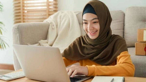 Smiling Muslim girl learning Quran online on a laptop, representing online Quran classes for kids at Al Zahra Quran Academy